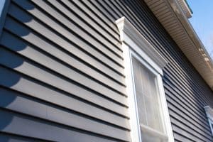 Close-up view of dark horizontal home siding surrounding a tall window with white trim and decorative molding.