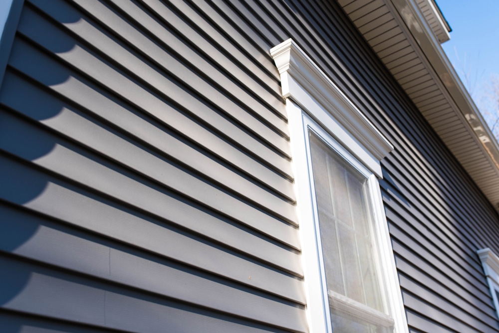 Close-up view of dark horizontal home siding surrounding a tall window with white trim and decorative molding.